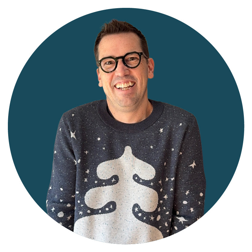 Jedd, the artist and designer, wearing a navy graphic knit sweater with a white spruce tree design