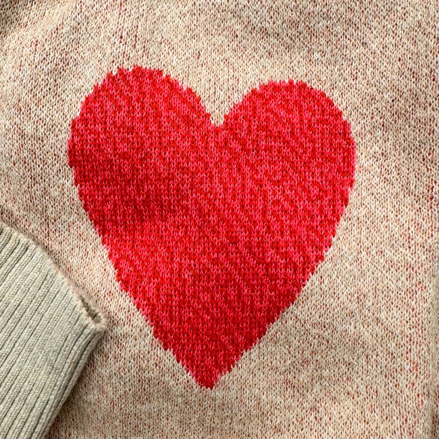 Close-up detail of the pink heart knit design on the sleeve of the heather cream Heart On My Sleeve sweater by Jedd