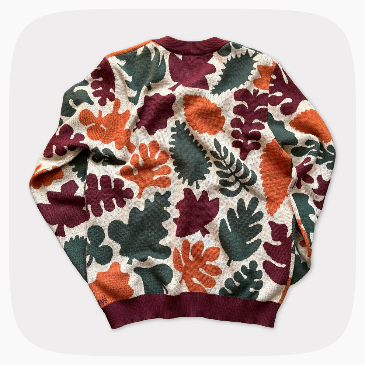 The back view of a graphic knit sweater with a light tan background and an allover pattern of green, red, and orange leaves.