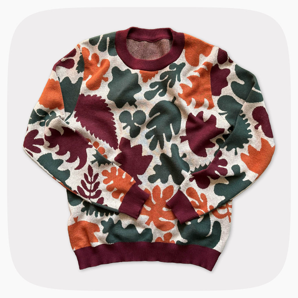 A graphic knit sweater with a light tan background and an allover pattern of green, red, and orange leaves.