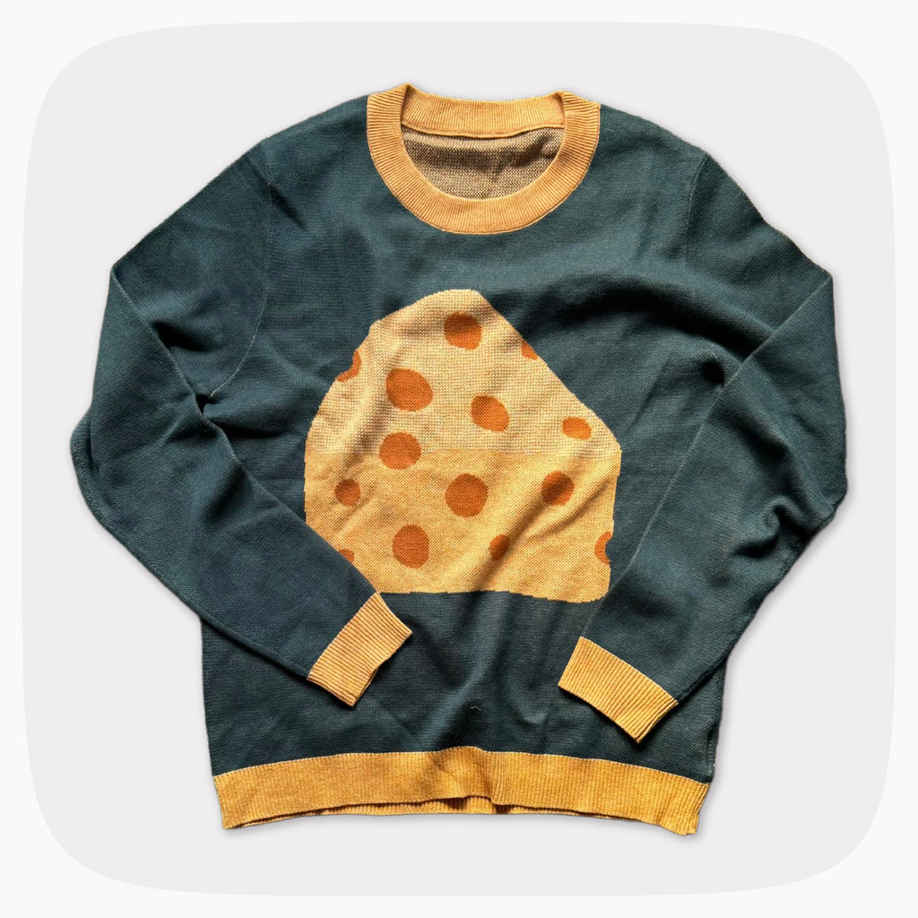 The front of a green graphic knit sweater with a big piece of cheese design on the center.