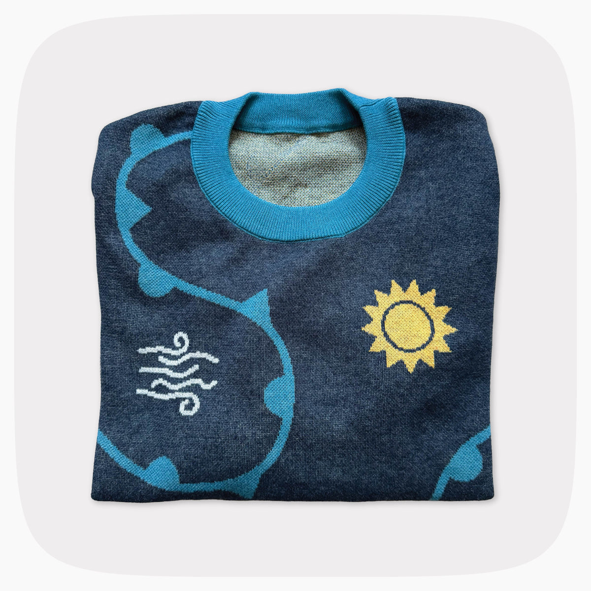 A folded blue graphic knit sweater with weather forecast shapes like the sunny, clouds, and snowflakes.