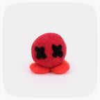 A small felted red ball with black X eyes and orange feet.