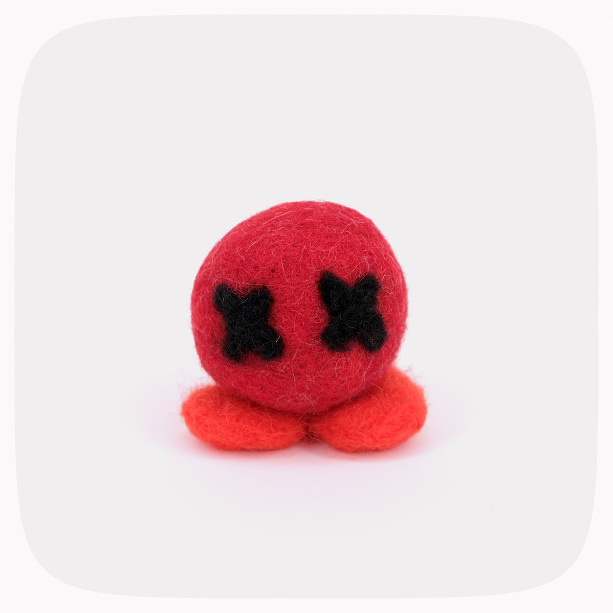 A small felted red ball with black X eyes and orange feet.