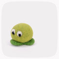 A green felted ball with eyes looking down and darker green feet.