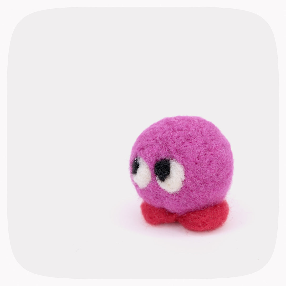 A small pink felted toy with red feet and big eyes.