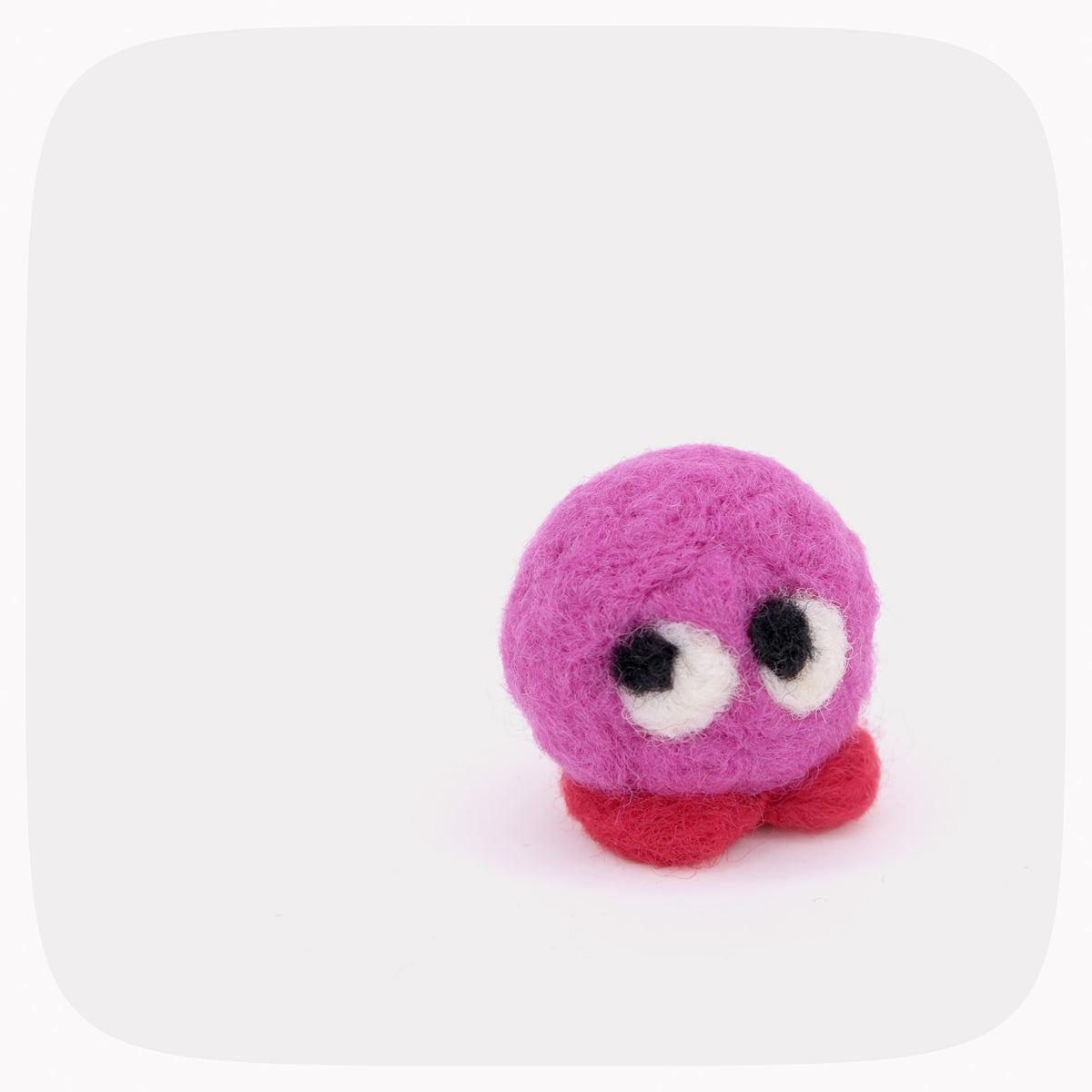 A small pink felted toy with red feet and big eyes.