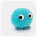 A soft blue felted toy character with darker blue feet and big eyes looking left.