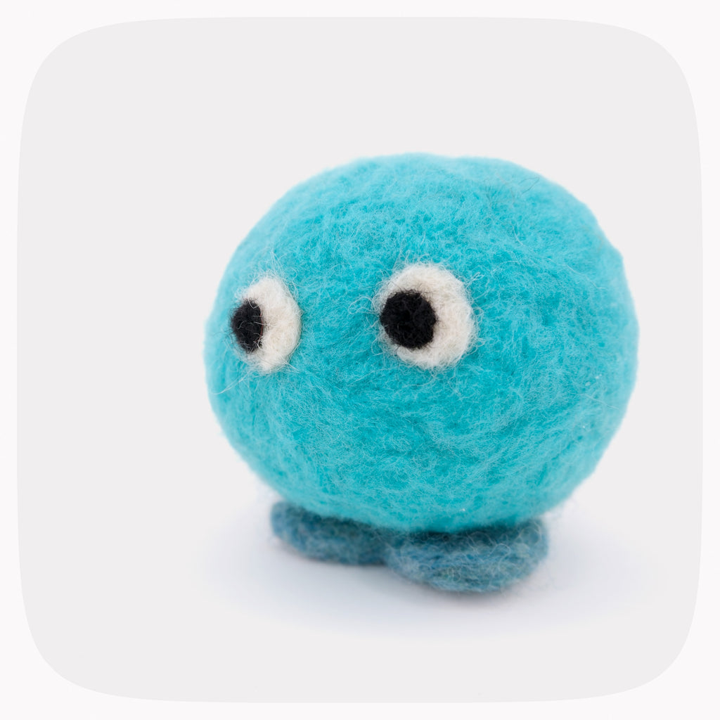 A soft blue felted toy character with darker blue feet and big eyes looking left.
