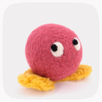 A bright red felted ball with eyes looking up and yellow feet.