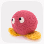 A bright red felted ball with eyes looking up and yellow feet.