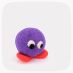 A purple felted ball with eyes looking down and bright orange feet.