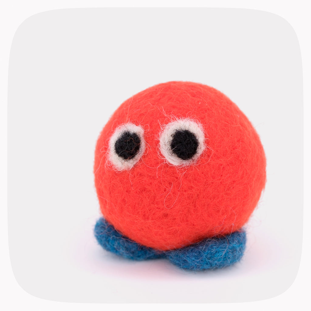 An orange felted ball with eyes and blue feet.