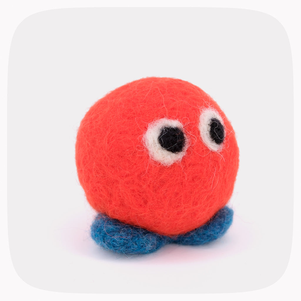 An orange felted ball with eyes and blue feet.
