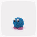 A small blue felted ball with eyes looking down and purple feet.