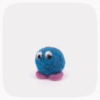 A small blue felted ball with eyes looking down and purple feet.