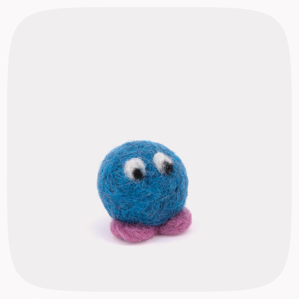 A small blue felted ball with eyes looking down and purple feet.