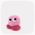 A pink felted ball with eyes looking up and red feet.