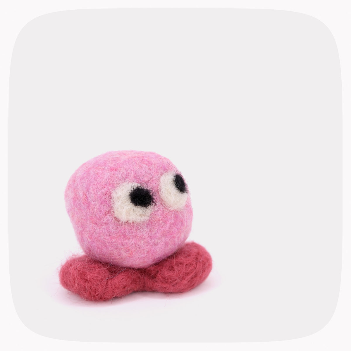A pink felted ball with eyes looking up and red feet.