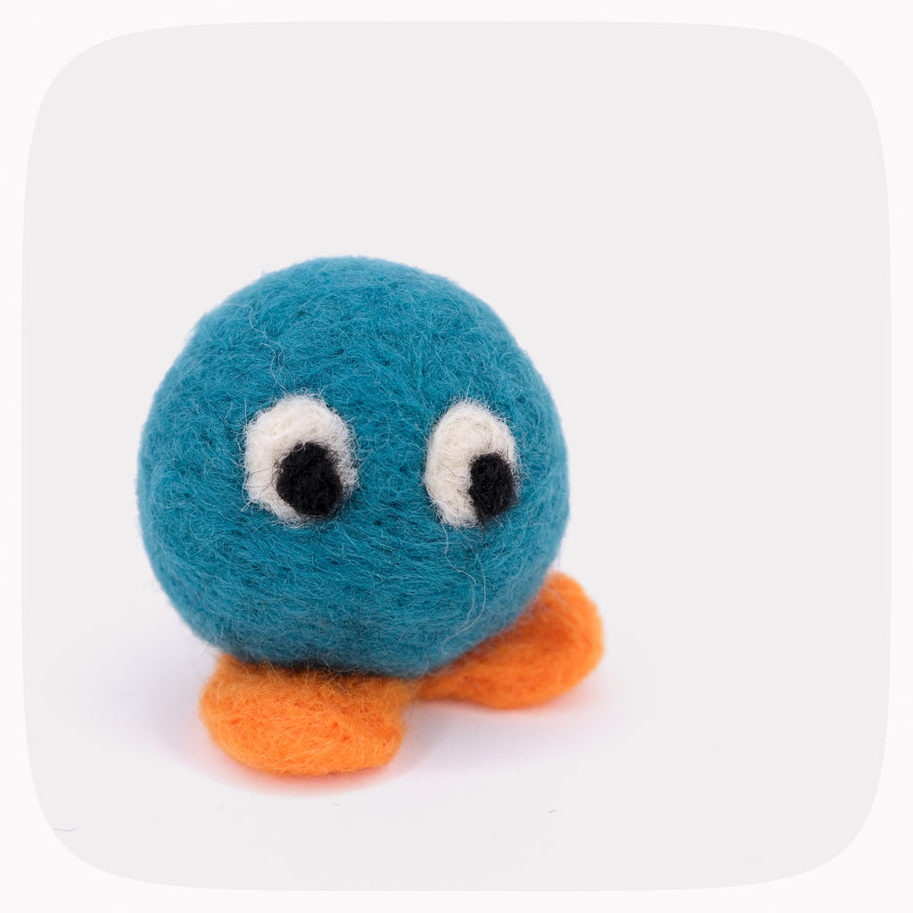 A teal blue felted ball with eyes looking down and bright orange feet.