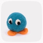 A teal blue felted ball with eyes looking down and bright orange feet.