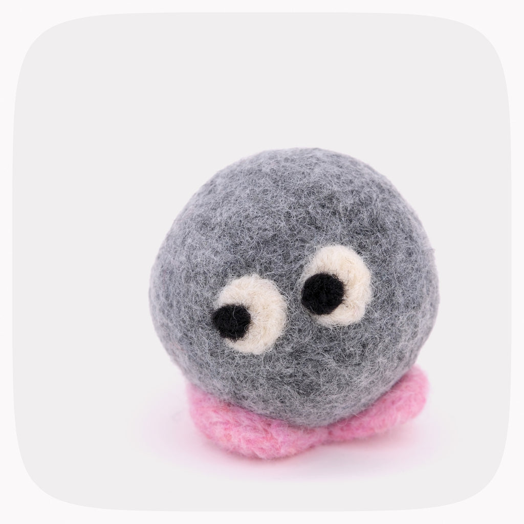 A gray felted ball with eyes looking left and pink feet.