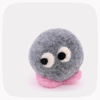 A gray felted ball with eyes looking left and pink feet.