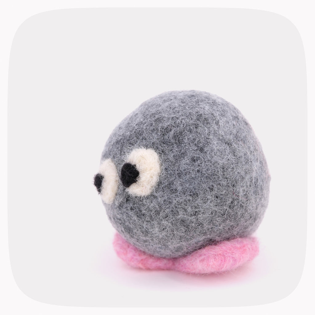 A gray felted ball with eyes looking left and pink feet.