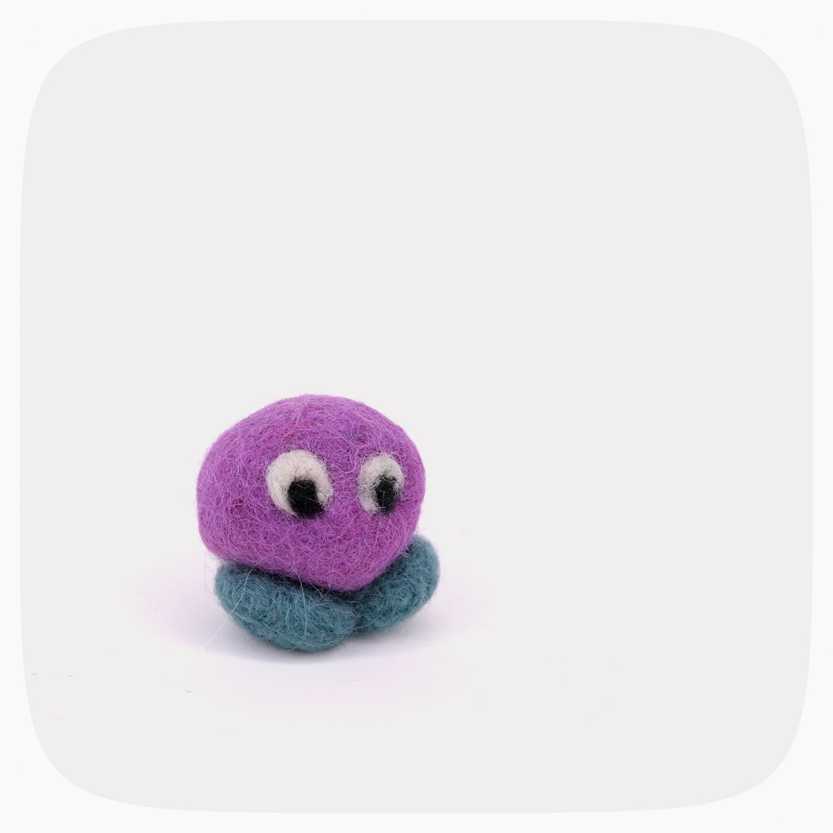 A small purple felted ball with blue feet and eyes looking right.