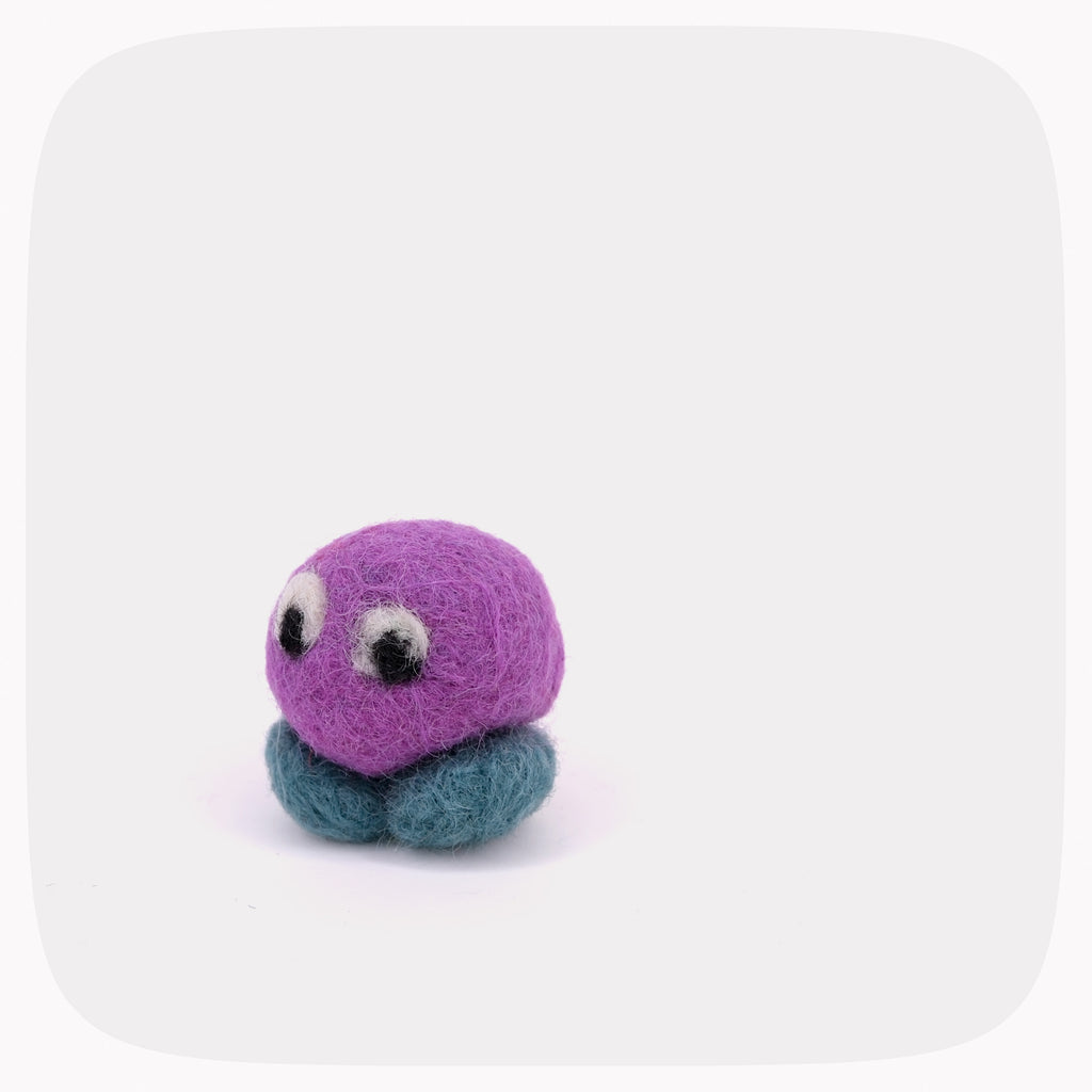 A small purple felted ball with blue feet and eyes looking right.