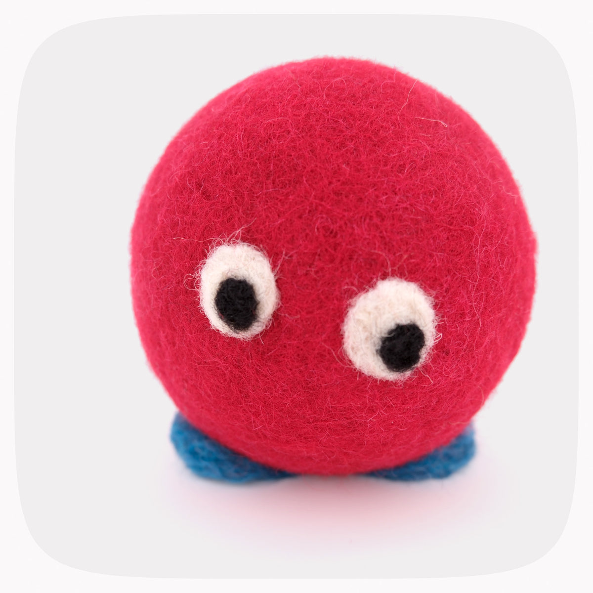 A felted red ball with blue feet and eyes looking down.