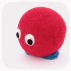 A felted red ball with blue feet and eyes looking down.