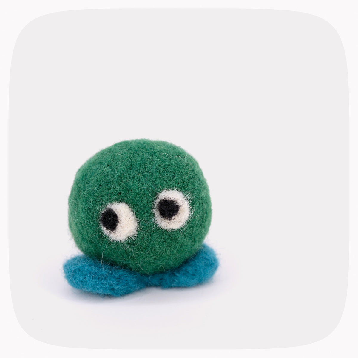 A small felted green ball with blue feet and eyes looking left.