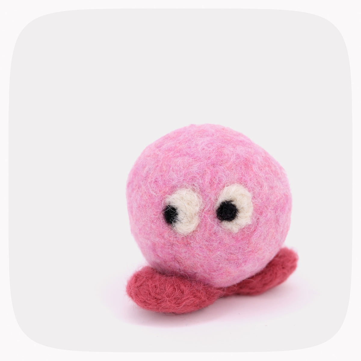 A small pink felted ball with red feet and eyes looking left.