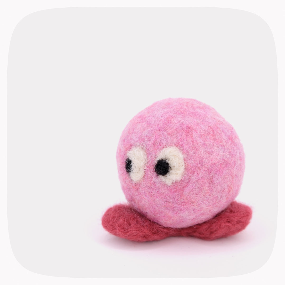 A small pink felted ball with red feet and eyes looking left.