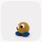 A small golden brown felted ball with blue feet and eyes looking left.
