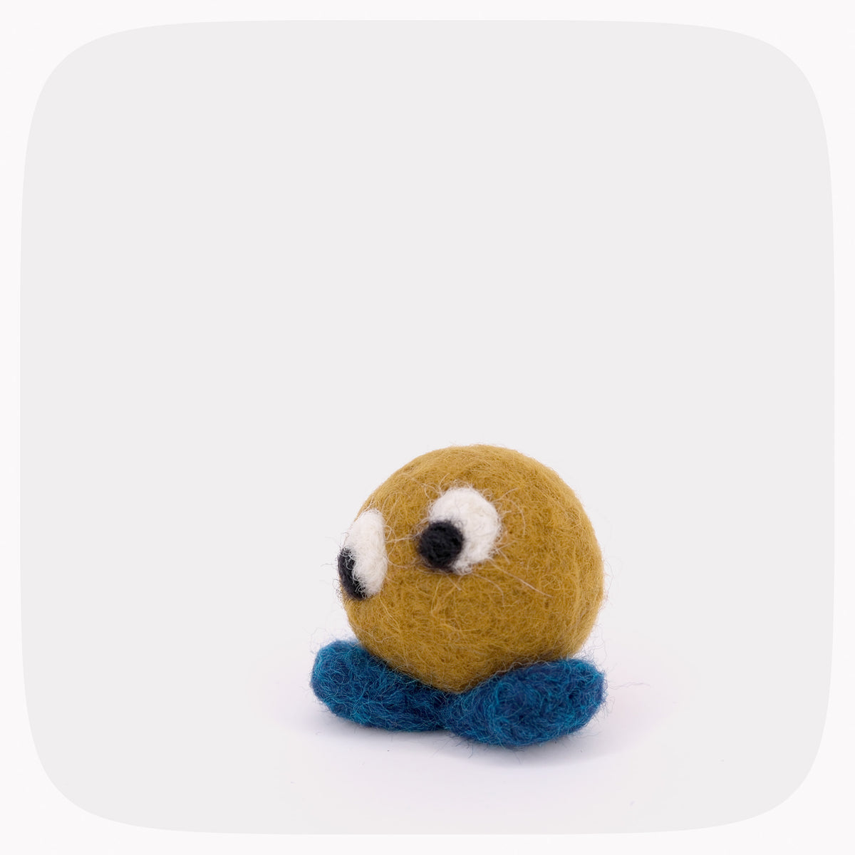 A small golden brown felted ball with blue feet and eyes looking left.