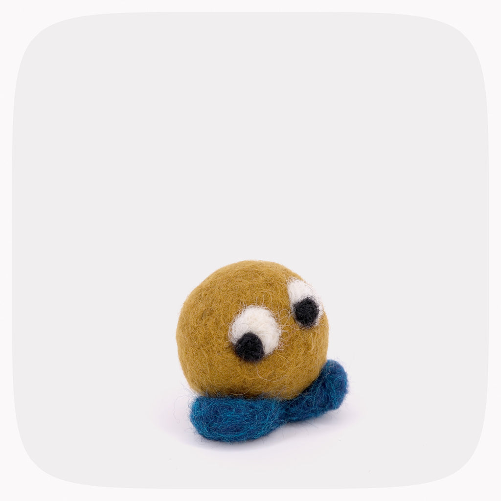 A small golden brown felted ball with blue feet and eyes looking left.