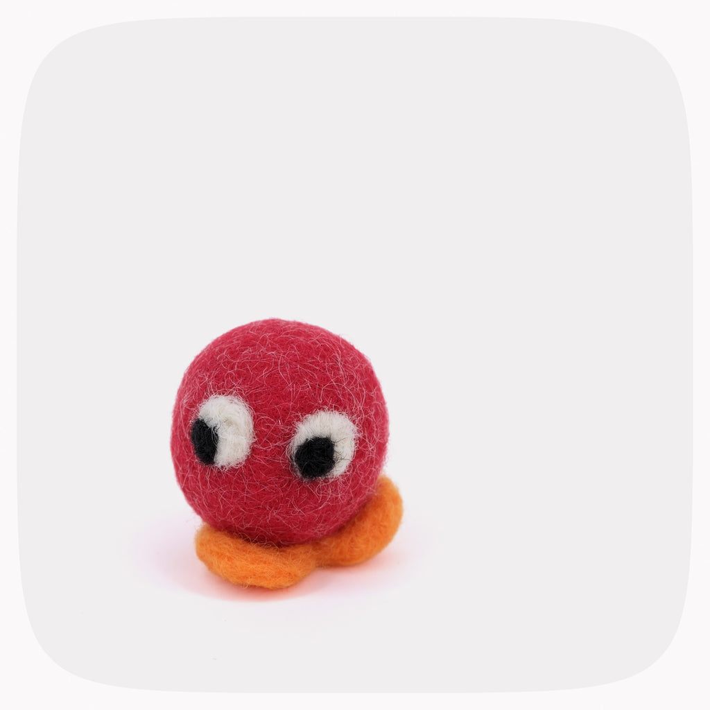 A small felt toy with a red round body, orange feet, and large white-and-black eyes, centered on a light gray background with rounded corners.