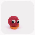 A small felt toy with a red round body, orange feet, and large white-and-black eyes, centered on a light gray background with rounded corners.