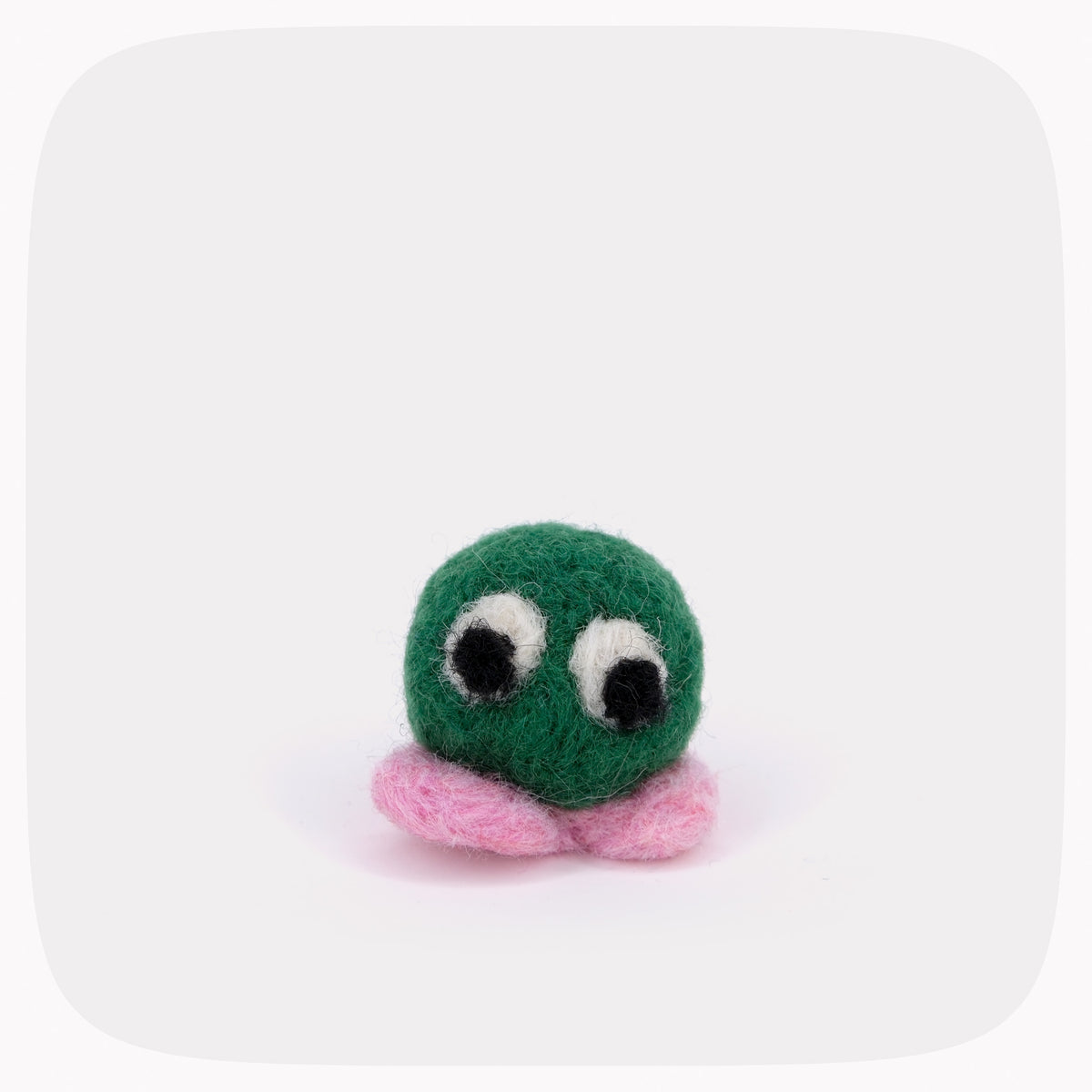 A small felt toy creature with a round green body, large black-and-white eyes, and pink feet, centered on a light gray background with rounded corners.