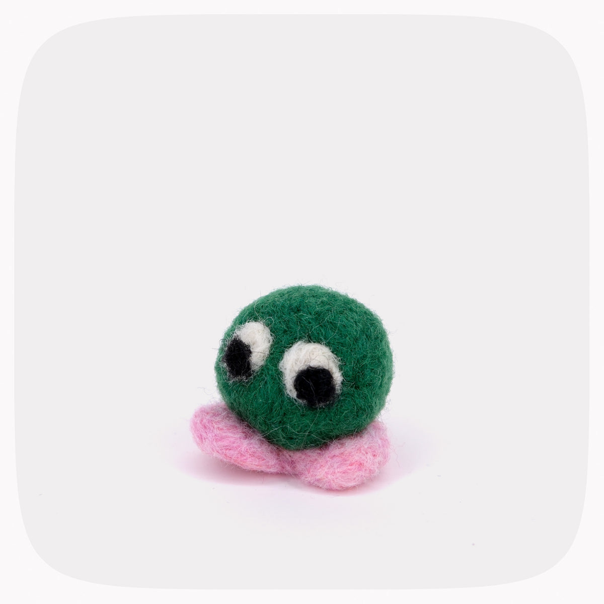 A small felted wool toy with a round green head, large white and black eyes, and pink feet, centered on a light gray background with rounded corners.