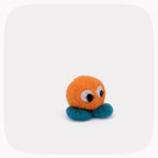 A small felt toy character with an orange round head, teal-blue feet, and large white-and-black eyes, centered on a light gray rounded-square background.