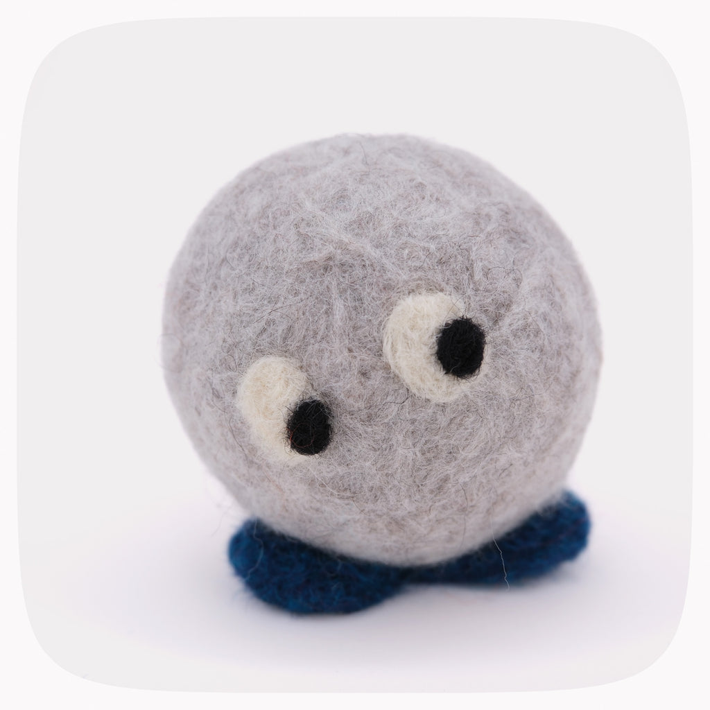 A small felted wool plush toy shaped like a round gray creature with large white and black eyes and dark blue felted feet, centered on a light gray background.