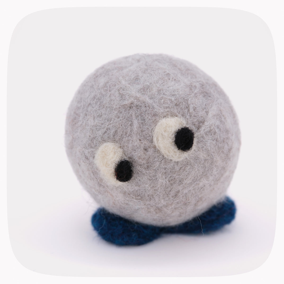A small felted wool plush toy shaped like a round gray creature with large white and black eyes and dark blue felted feet, centered on a light gray background.