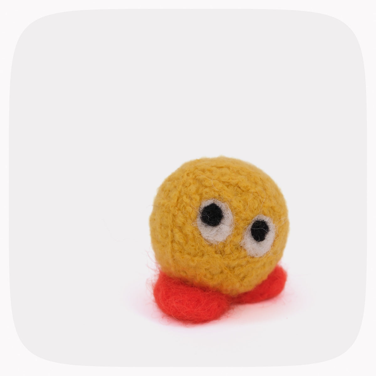 A small handmade felt toy with a round yellow head, large black and white eyes, and red feet, centered on a light gray background with rounded corners.