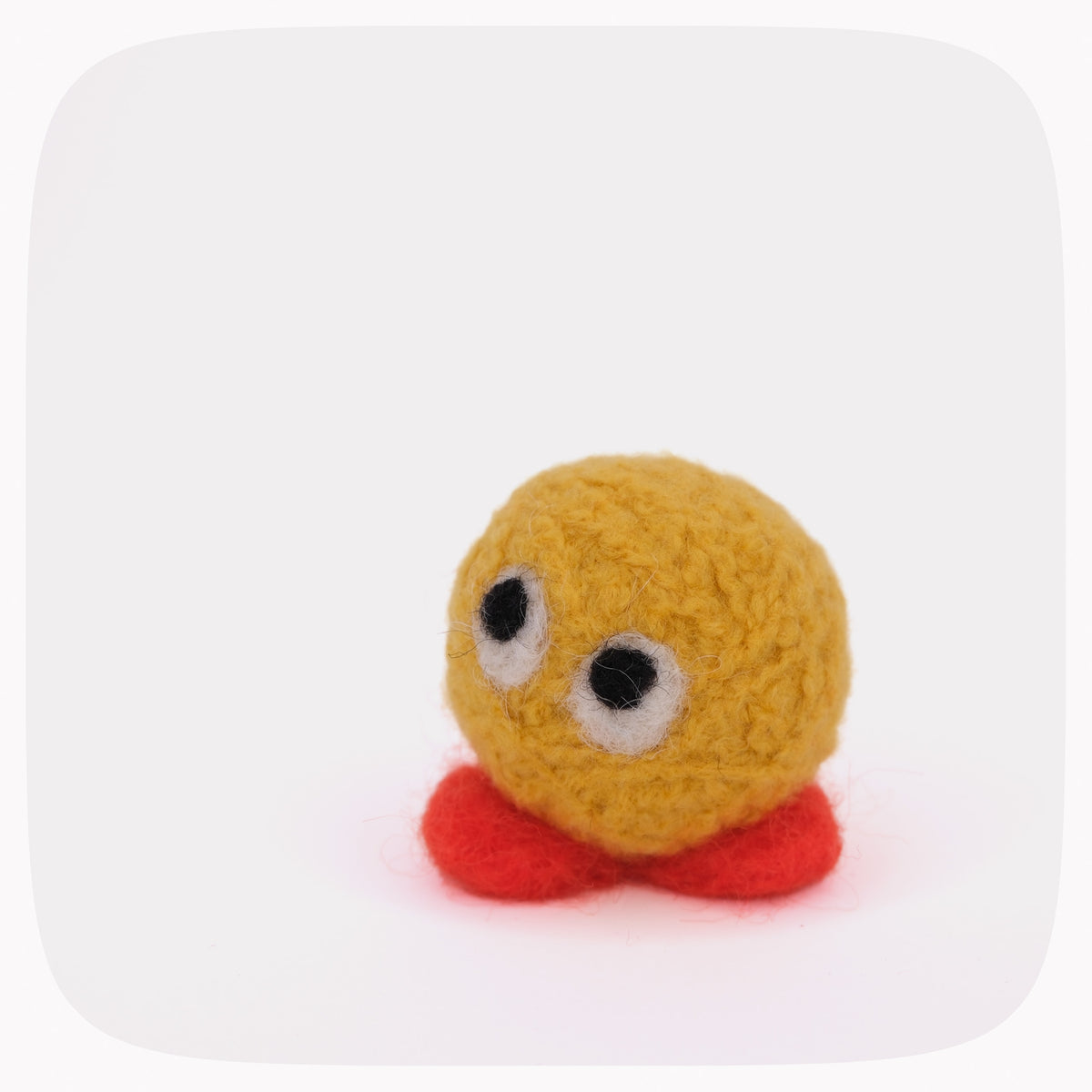 A small handmade felt toy with a round yellow head, two large black-and-white eyes, and red feet, photographed on a plain white background.