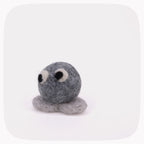 A small felted wool toy in shades of gray with black and white eyes, photographed on a clean white background with rounded corners.