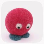 A small felt toy character with a round red head, two white eyes with black pupils, and two blue feet, photographed on a clean white background.