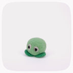 A small green felt toy with large white eyes and dark bead eyes, standing on a dark green felt base against a white background with rounded corners.